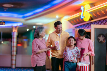 Family, parents, children and grandma holding popcorn and drinking water chatting cheerfully before the movie.