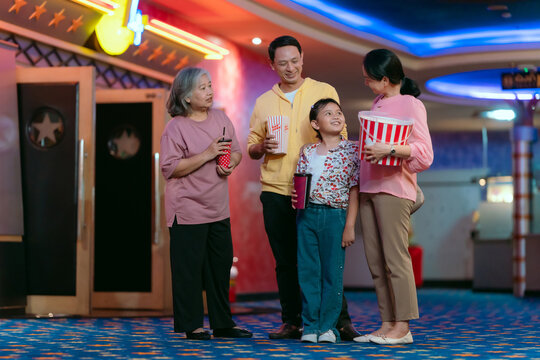 Family, parents, children and grandma holding popcorn and drinking water chatting cheerfully before the movie.