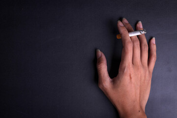 Close up hand holding a cigarette on a dark background with copy space for your text, message or ads.