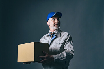 Portrait of an elderly Caucasian delivery staff in work clothes holding a  cardboard box luggage.