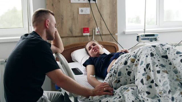 Man is holding his pregnant wife's hand while she's tested on the medical equipment. Diagnostics and fetal heart monitoring before the labor.