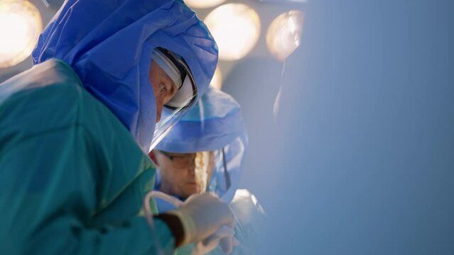 Focused faces of doctors wearing helmets in surgery room. Medics perform orthopedic operation.
