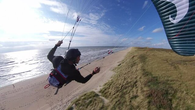Following action shot of an extreme paraglider skimming across the dunes along a beach showing amazing skill and daring