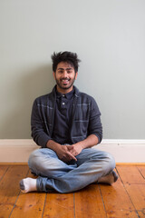 Asian man sitting on floor against green wall.