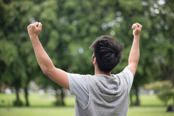 Asian man standing with arms raised outdoors.
