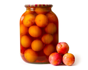 Canned plums in a glass jar on a white background. In the foreground are fresh plums. Homemade canned fruit.