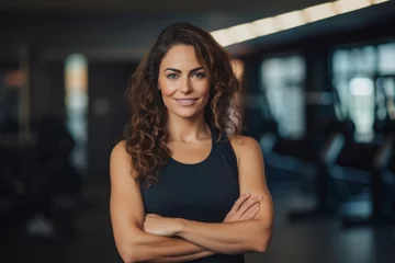 Gordijnen Portrait of smiling young woman standing with arms crossed in fitness center © igolaizola