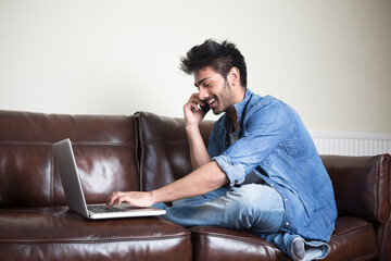 Indian Man using a laptop and phone at home.