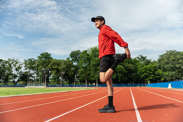 Young Asian man stretching his leg warm up before workout outdoor running track background. The man in sportswear exercises outside in the morning for health and wellbeing.