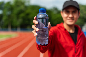 Focus drinking water bottle. Athletic young asian man holding drinking water bottle and show to...