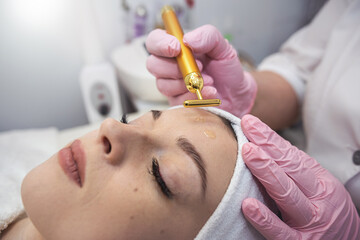 beautician makes procedure use vibrating electric facial massager for her female clien