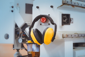Yellow protective ear muffs hang on machines in heavy industrial plants..