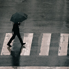 silhouette of a person walking with umbrella at a crossing