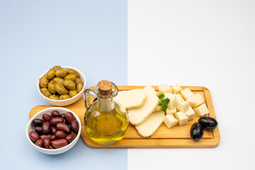Varieties of pickled olives, sliced halloumi cheese with herbs and a bottle of extra virgin olive oil on a wooden tray as a traditional Cypriot export concept