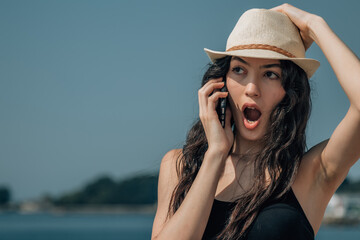 girl with astonishment gesture on the beach talking with the smartphone - obrazy, fototapety, plakaty