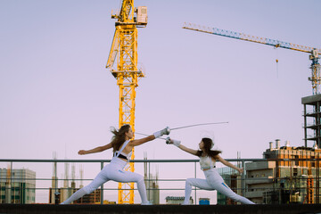 Two fencers woman practice on a rooftop with the city in the background.