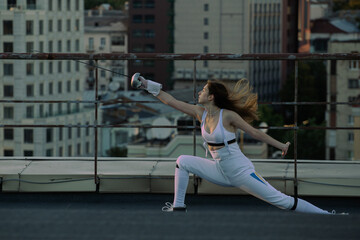 Two fencers woman practice on a rooftop with the city in the background.
