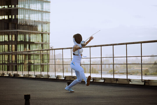 Two fencers woman practice on a rooftop with the city in the background.