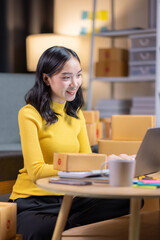 Startup small business entrepreneur or freelance Asian woman using a laptop with box in night, Young success Asian woman with her hand lift up, online marketing packaging box and delivery, SME concept