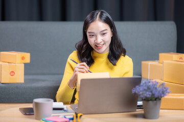 Startup small business entrepreneur or freelance Asian woman using a laptop with box in night, Young success Asian woman with her hand lift up, online marketing packaging box and delivery, SME concept