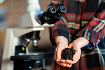 Female farmer holding soil, doing soil tests in her home laboratory. Looking at soil life and health