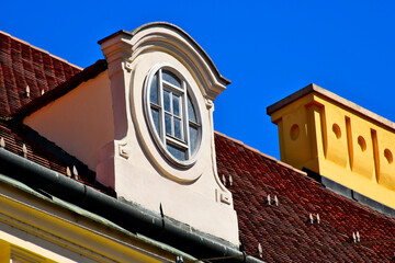 sloped red clay residential roof with decorative dormer. oval wood window. yellow stucco ornate...