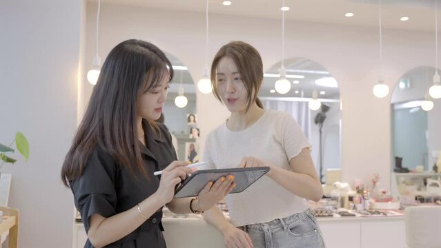 태블릿으로 유행하는 스타일을 보여주는 메이크업샵 원장과 선택하는 고객 