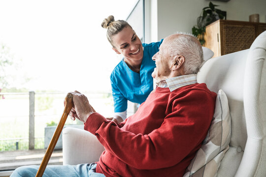 Happy nurse taking care of senior man sitting in armchair at home