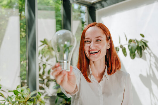 Happy Businesswoman Looking At Light Bulb In Office