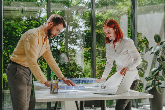 Happy businesswoman having discussion with colleague over solar panel prints in office
