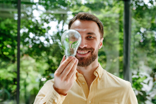 Happy businessman looking through light bulb in office