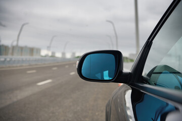 Black wing mirror of modern car. Left side car rear-view mirror and empty highway.