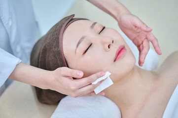 Obraz na płótnie Canvas 아시아 한국의 젊은 한국여성 모델은 거즈를 이용해 스파 또는 피부관리전문점 또는 피부과 병원의 침대에 누워서 전문관리사에게 머리와 얼굴을 관리를 받음