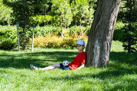 Boy sitting under a tree in summer with a football, Georgia