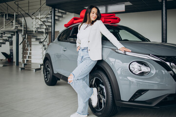 Woman in car showroom standing by her new car with red bow