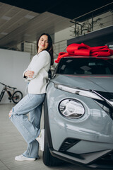 Woman in car showroom standing by her new car with red bow