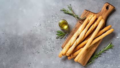 Fresh baked grissini bread sticks on wooden cutting board with olive oil and herbs rosemary and...