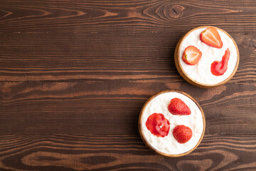 Grained cottage cheese with strawberry jam on brown wooden, top view, copy space.