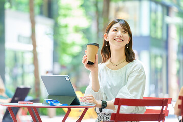 コーヒーを飲みながら街角でタブレットPCを操作する女性