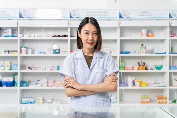Fototapeta na wymiar Happy handsome asian female pharmacist wearing lab coat standing with arms crossed and looking at camera, She feels good, trustworthy and proud of his work in the pharmacy drugstore.