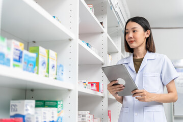 Medical pharmacy and healthcare. Beautiful asian pharmacist female wearing lab coat working checking stock of medical product, medicine and supplements on shelf in modern drugstore.