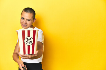 Young woman eating popcorn, cinema concept, yellow backdrop