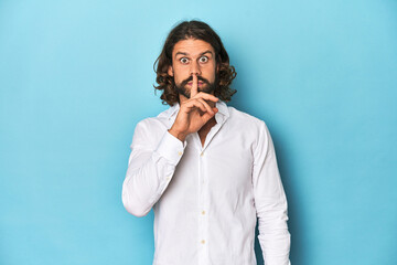 Bearded man in a white shirt, blue backdrop keeping a secret or asking for silence.