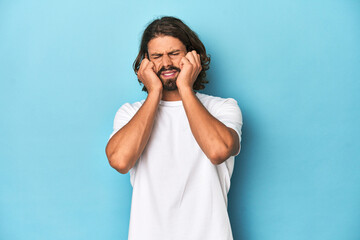 Bearded man in a white shirt, blue backdrop whining and crying disconsolately.