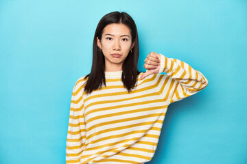 Fototapeta premium Asian woman in striped yellow sweater, showing a dislike gesture, thumbs down. Disagreement concept.