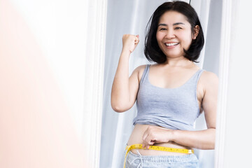 happy Asian woman success on dieting and weight loss measuring her waist with tape measure smiling...