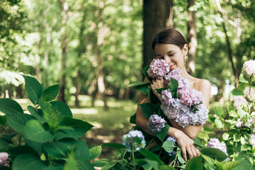 Portrait of beautiful young woman standing posing in park with blooming flowers Hydrangea garden....
