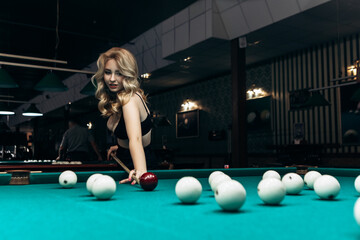 Blond woman playing enjoying billiard, hold cue hit white billiard balls on table with green...