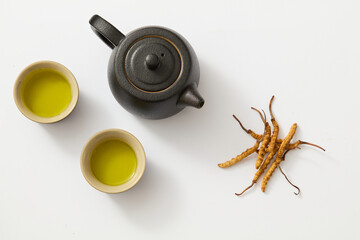 On the white background, black teapot with two tea cups decorated with dried cordyceps. Scene for advertising product with ingredient with cordycep, am ingredients used in traditional Chinese medicine