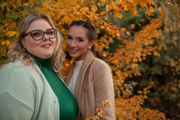 Multiracial female people  with different bodies and hairs walking in the fall parks together.  Friends wearing warm fashion clothes, knitted sweaters.